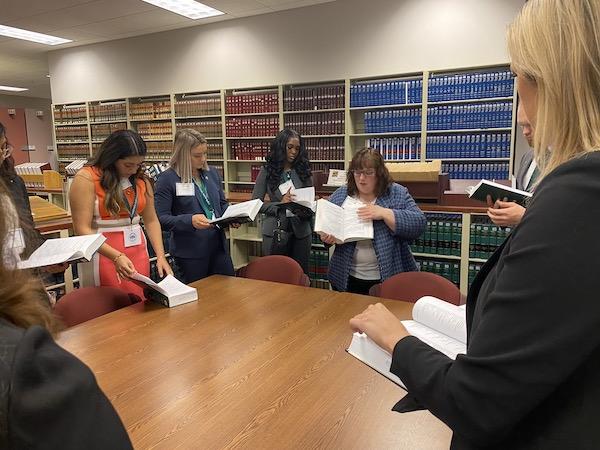 一个法律图书管理员和一群法律学生站在一张桌子旁, 给他们看她手里拿着的一本书的一部分.